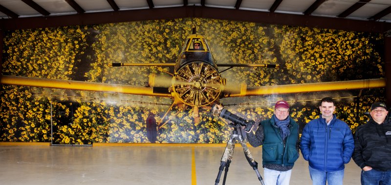 This image of Allen Chorman flying his 600 horsepower Thrush over a sunflower field is 1,200 square feet of self-adhesive vinyl. Shown (l-r) are photographer Kevin Fleming, Jeff Chorman and Jason Dean of JD Signs in Felton. KEVIN FLEMING PHOTO